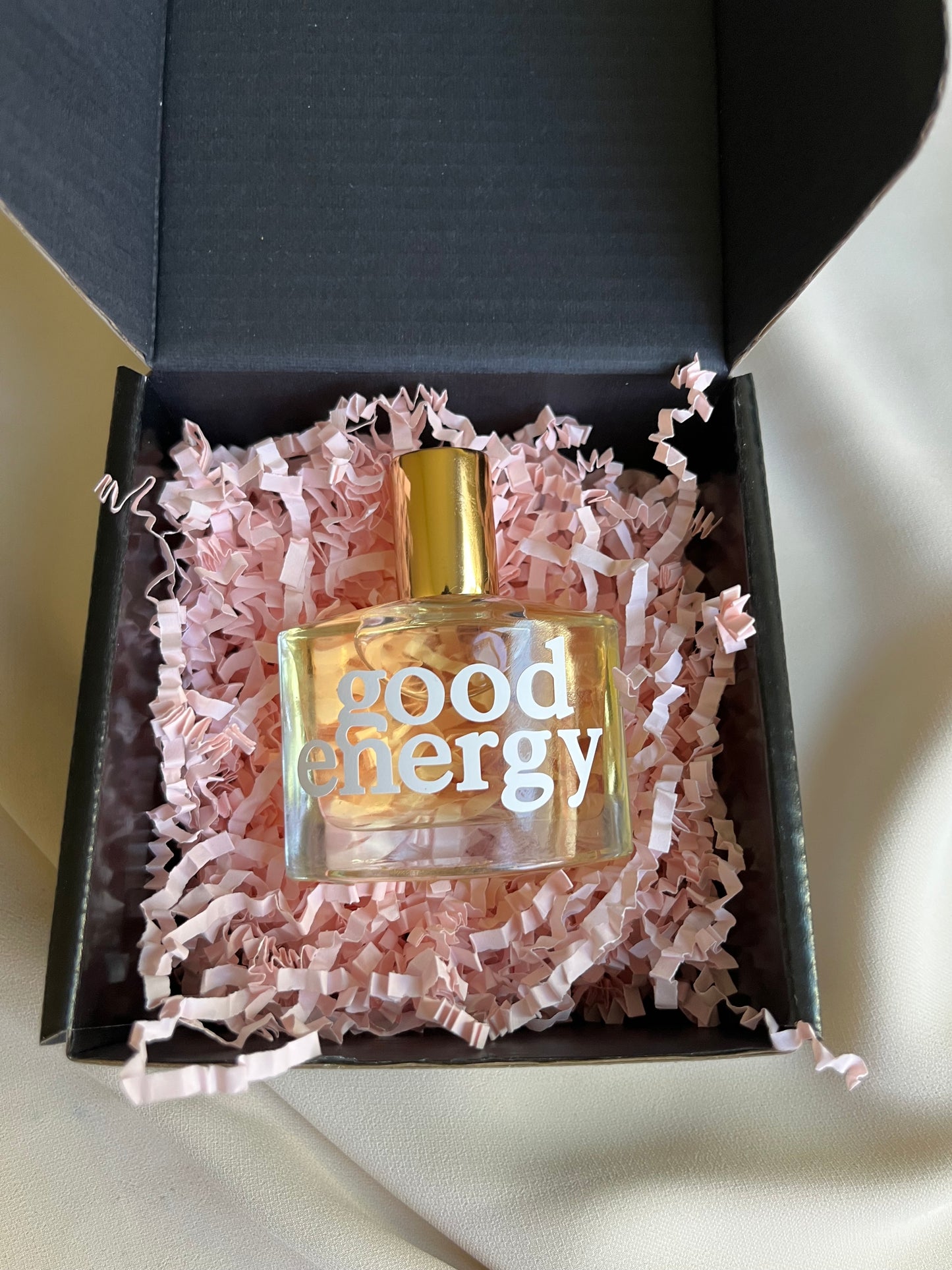 Perfume bottle with gold cap and clear label in a black box with pink tissue paper