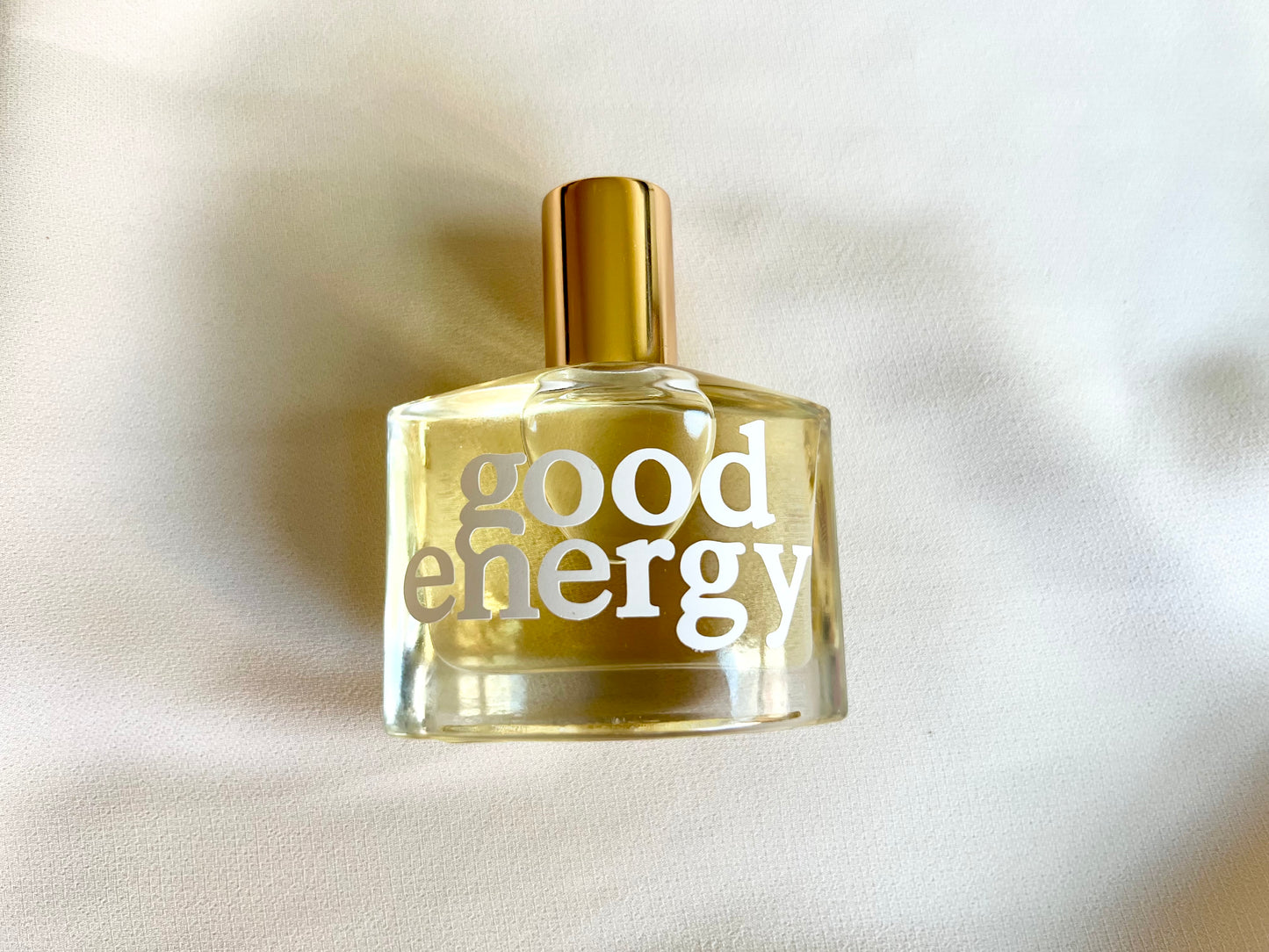 Perfume bottle labeled 'good energy' on a beige fabric background